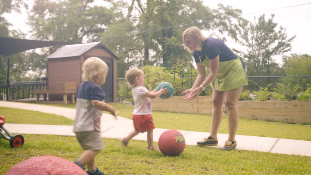 2 toddlers and teacher play with red ball on playground 1